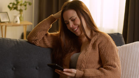 Woman-Sitting-On-Sofa-At-Home-Using-Mobile-Phone-To-Check-Social-Media-Message-And-Scrolling-Online-15